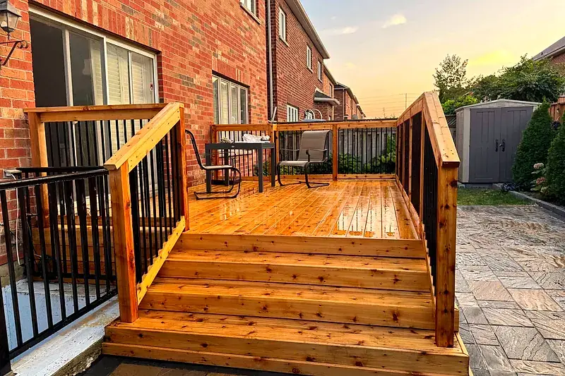 A new cedar deck with black railings and wide stairs at the back of a brick home